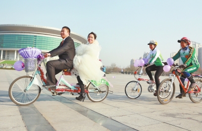 氣球和鮮花裝點(diǎn)的雙人自行車，新郎郝幸福載著美麗新娘回家。